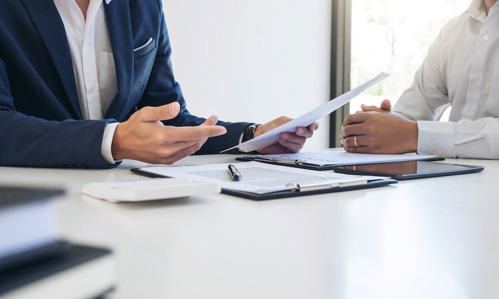 A car dealer sitting at a table with a customer, discussing paperwork